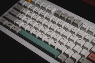 A mechanical keyboard with a close-up view showing a variety of keycaps featuring different colors. The layout includes standard alphanumeric keys and function keys, with a distinctive light green space bar and some other keys in shades of beige, gray, and pink.