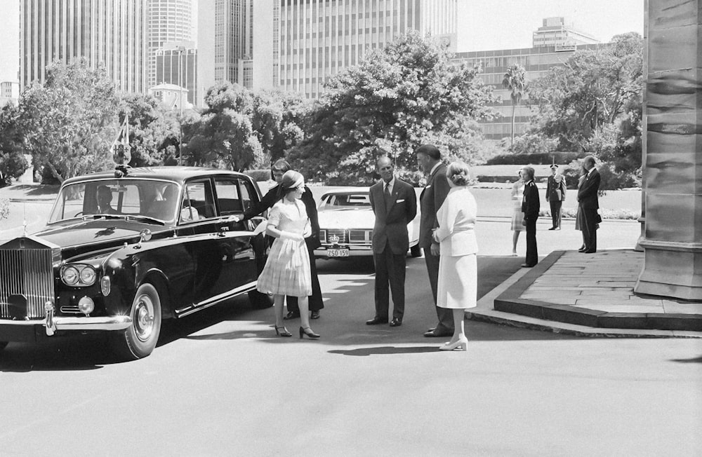 a black and white photo of people standing next to a car
