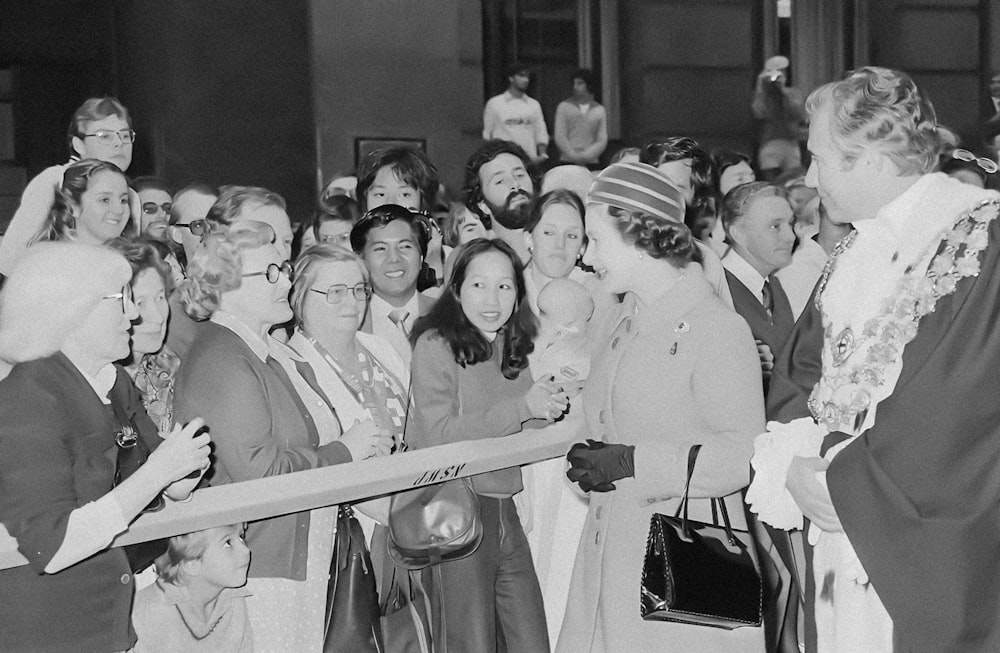 a crowd of people standing around a woman cutting a ribbon