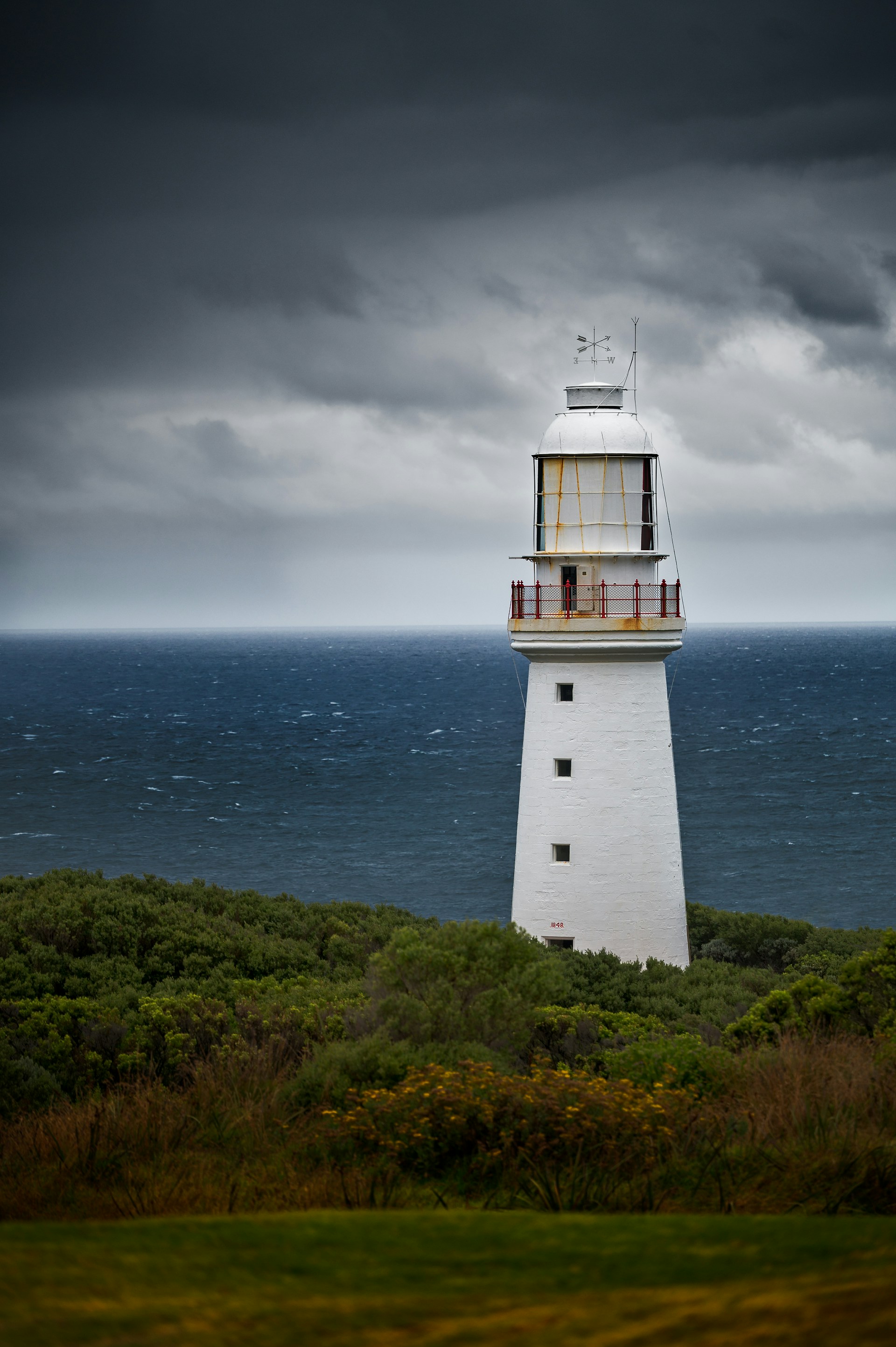 a lighthouse on a hill overlooking the ocean under a cloudy sky