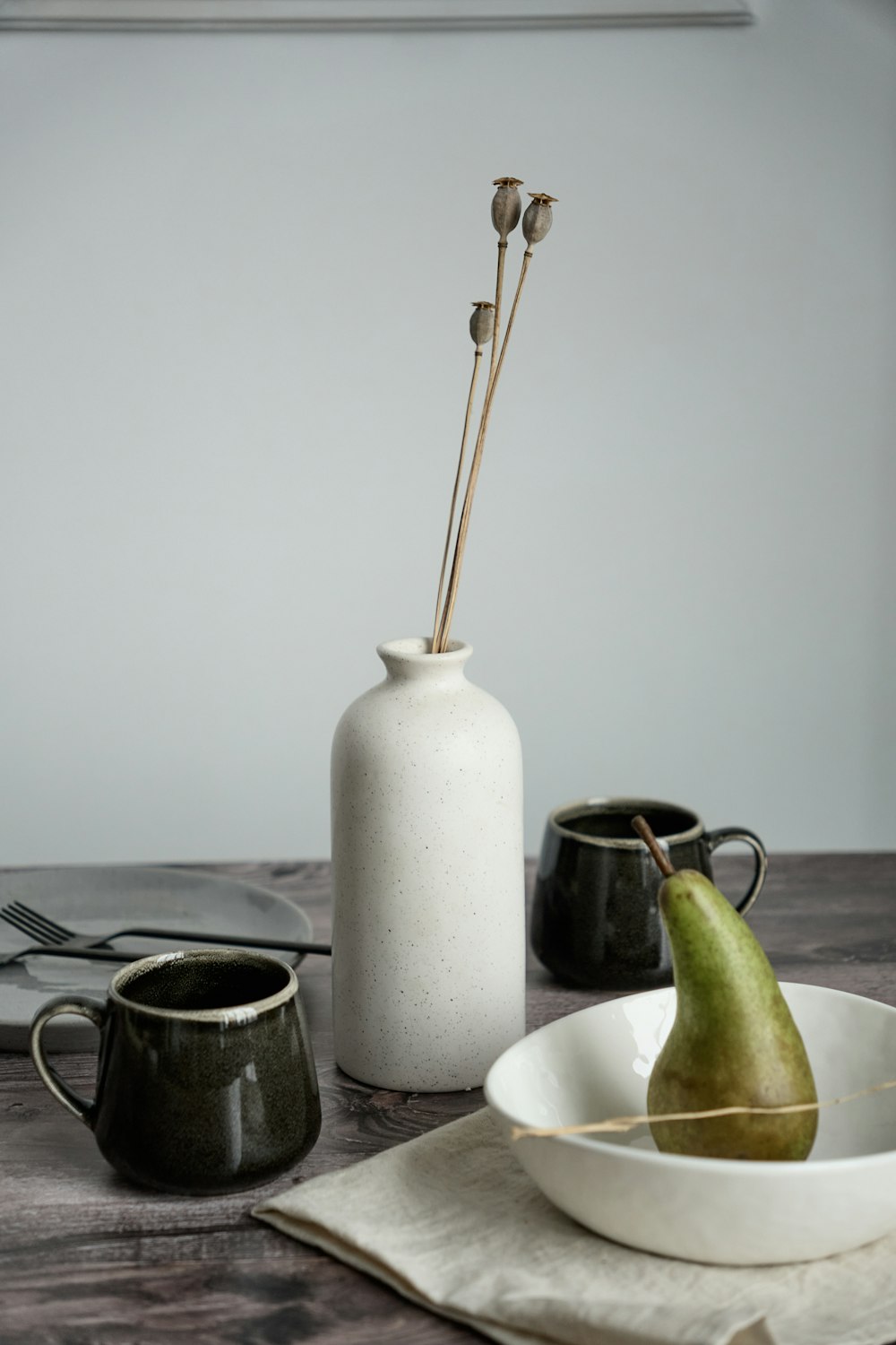 a table topped with a white vase filled with a green pear