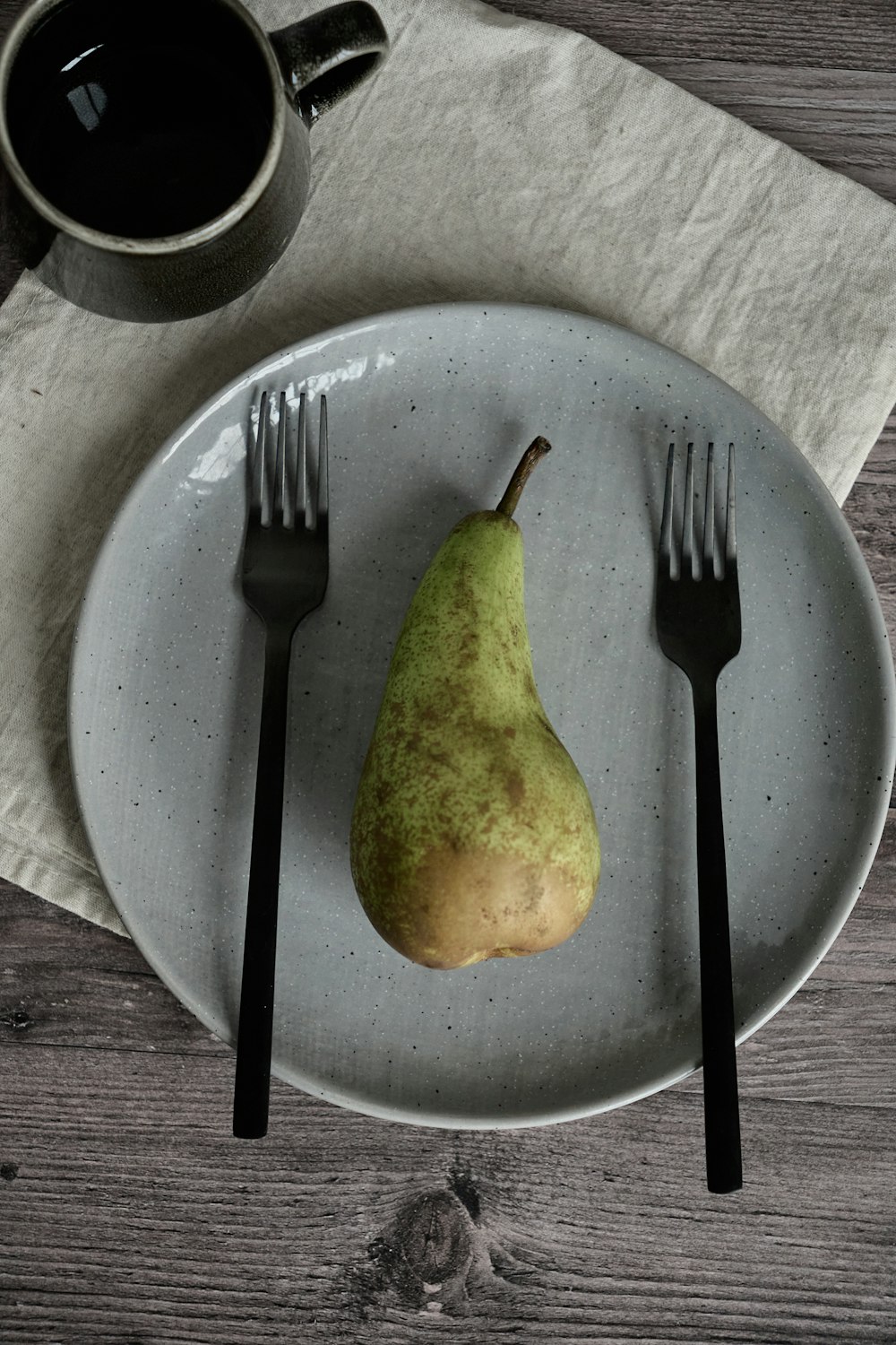 a pear and fork on a plate with a cup of coffee