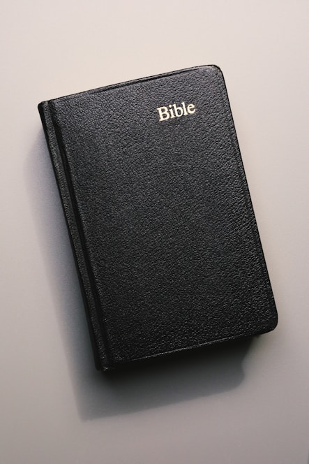 A black leather-bound Bible with 'Bible' written in gold lettering on the cover, lying on a flat, neutral-colored surface.