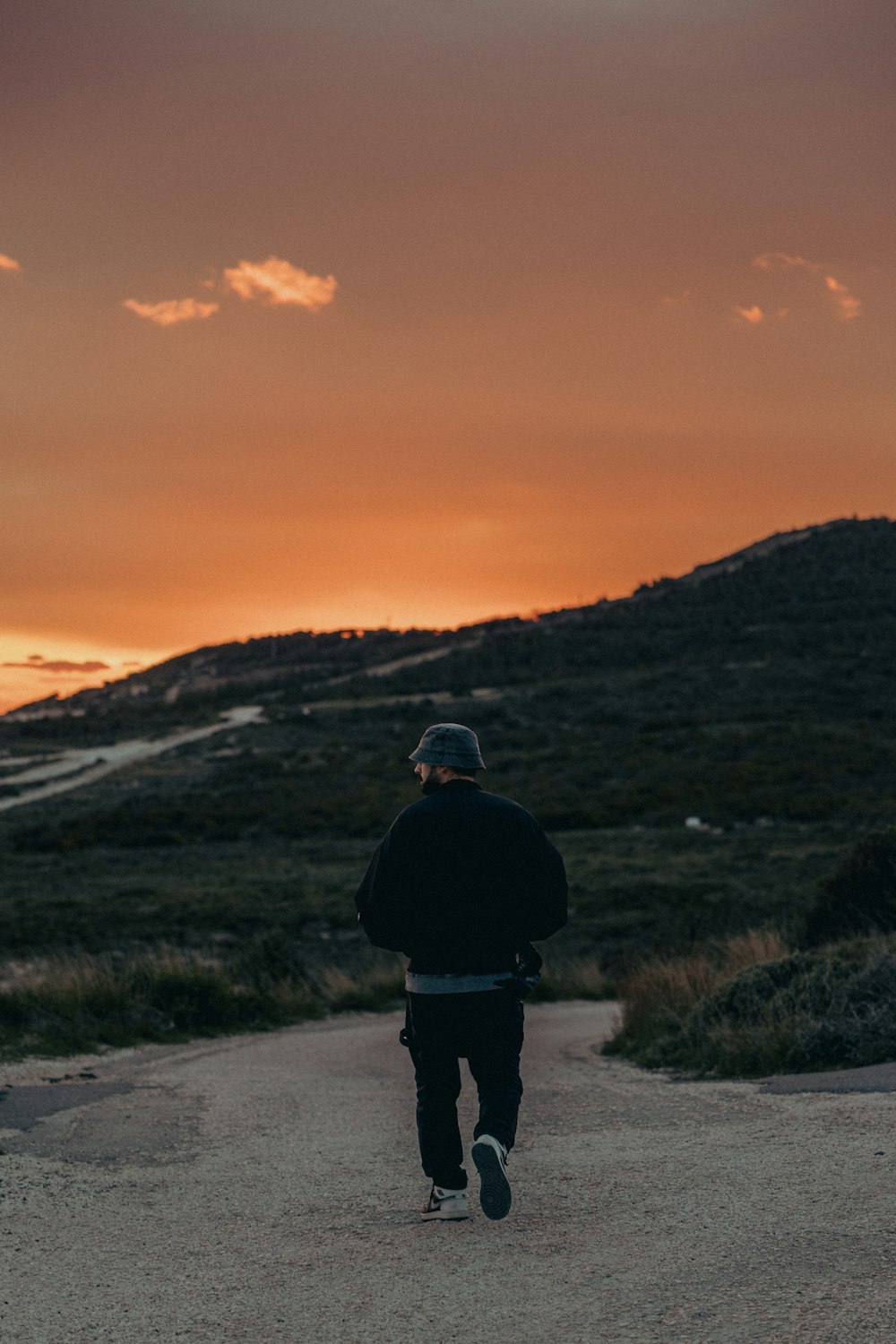 a man walking down a dirt road at sunset