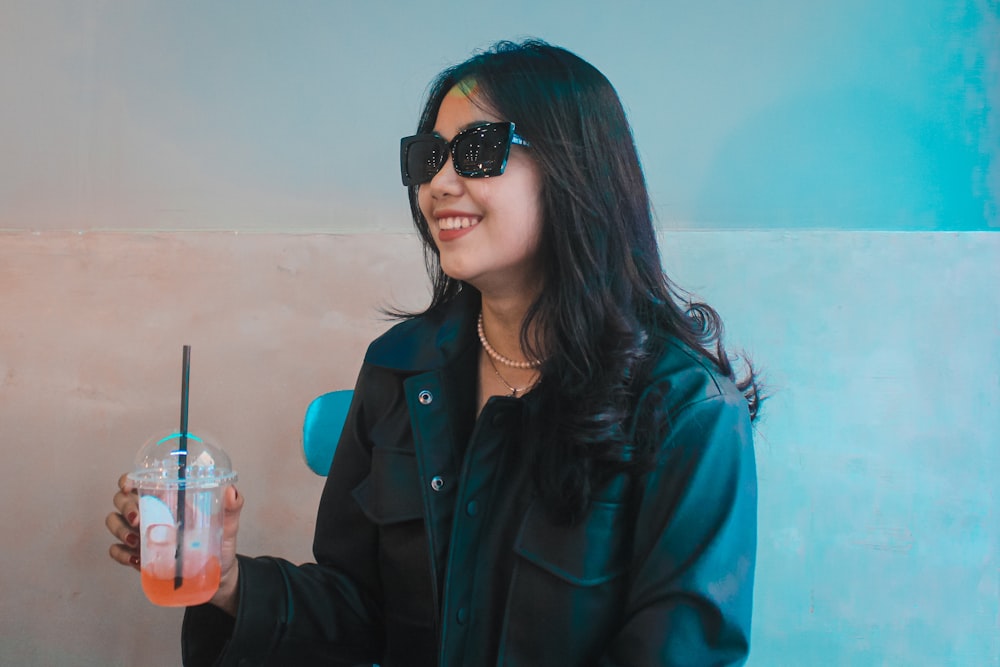 a woman wearing sunglasses holding a drink in her hand