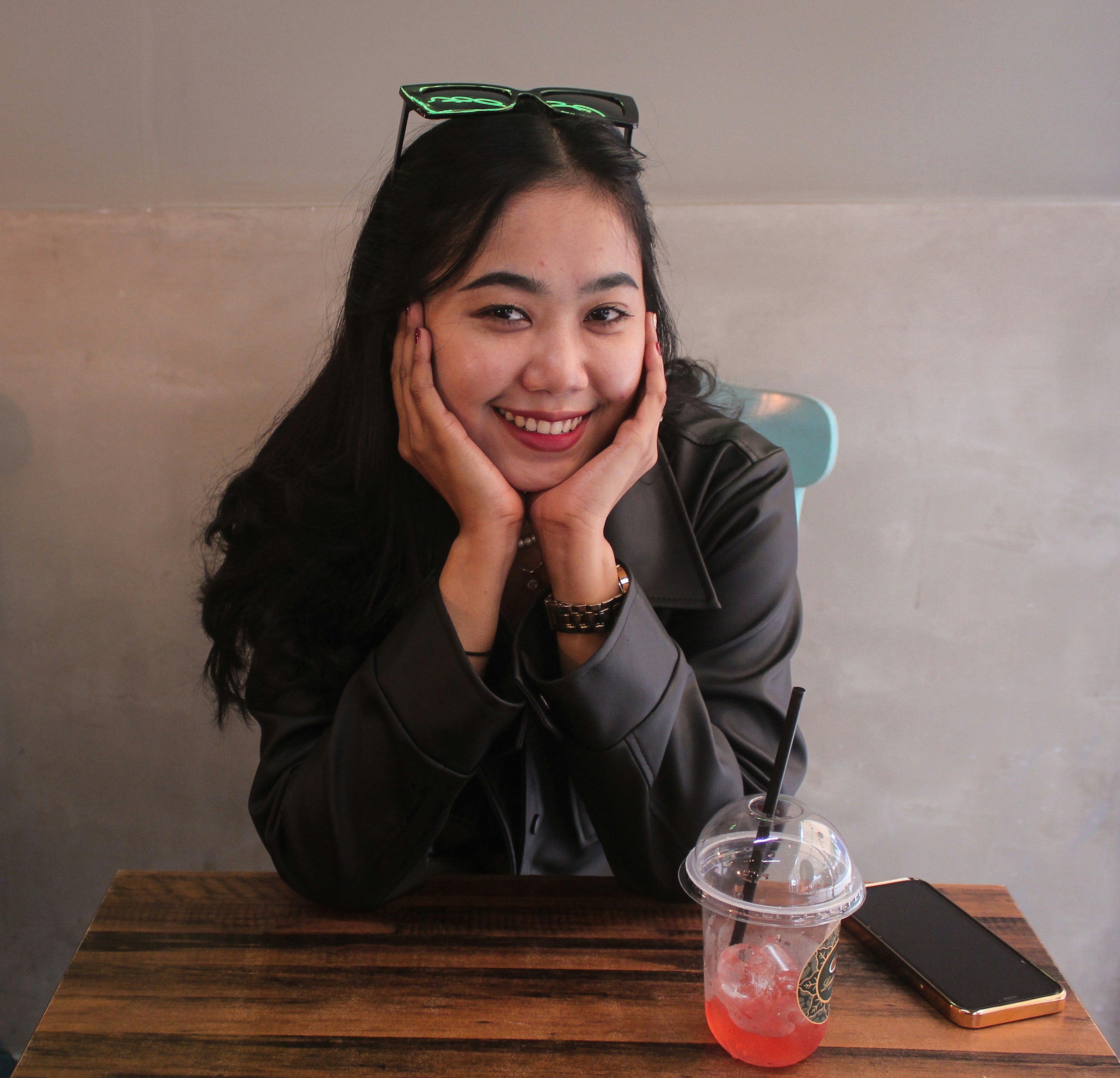 seorang wanita duduk di meja dengan minuman dan ponsel