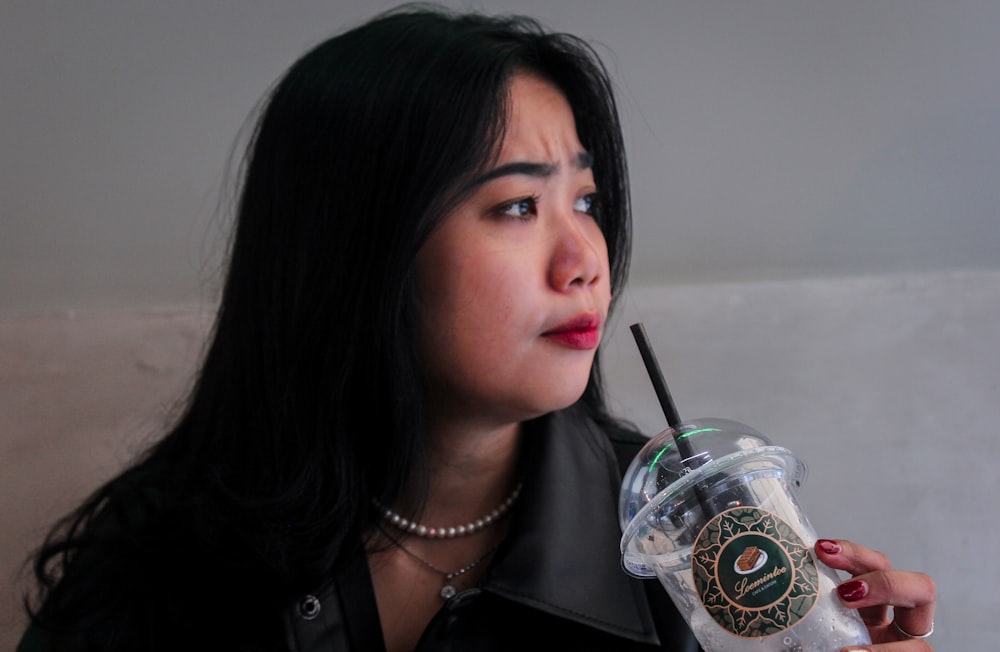 Une femme tenant une tasse Starbucks avec une paille dans la bouche