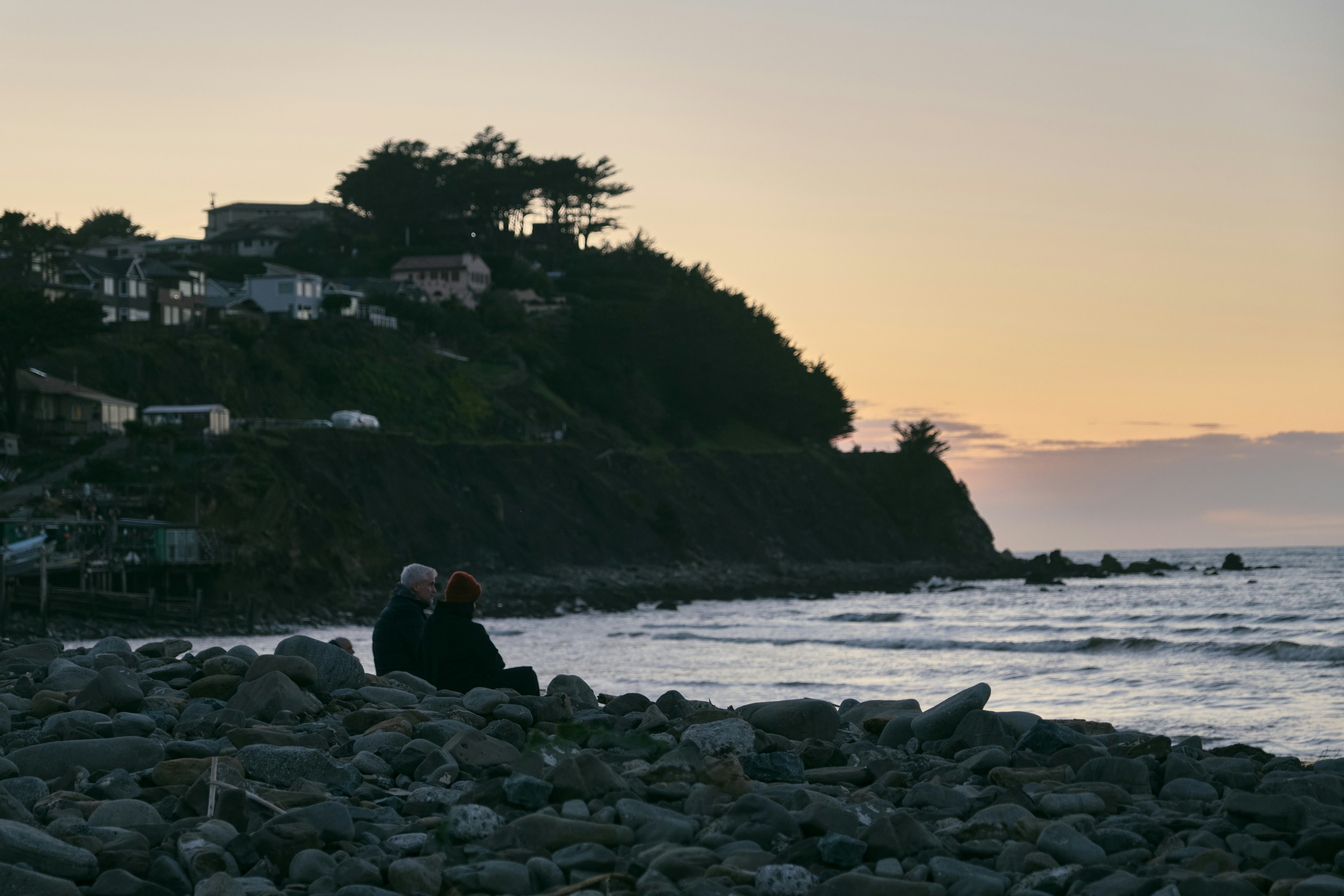 a couple of people sitting on top of a rocky beach