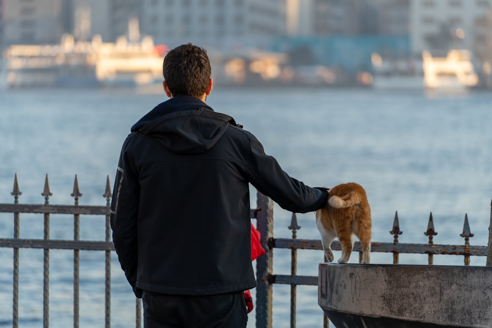 a man standing next to a fence with a cat on top of it