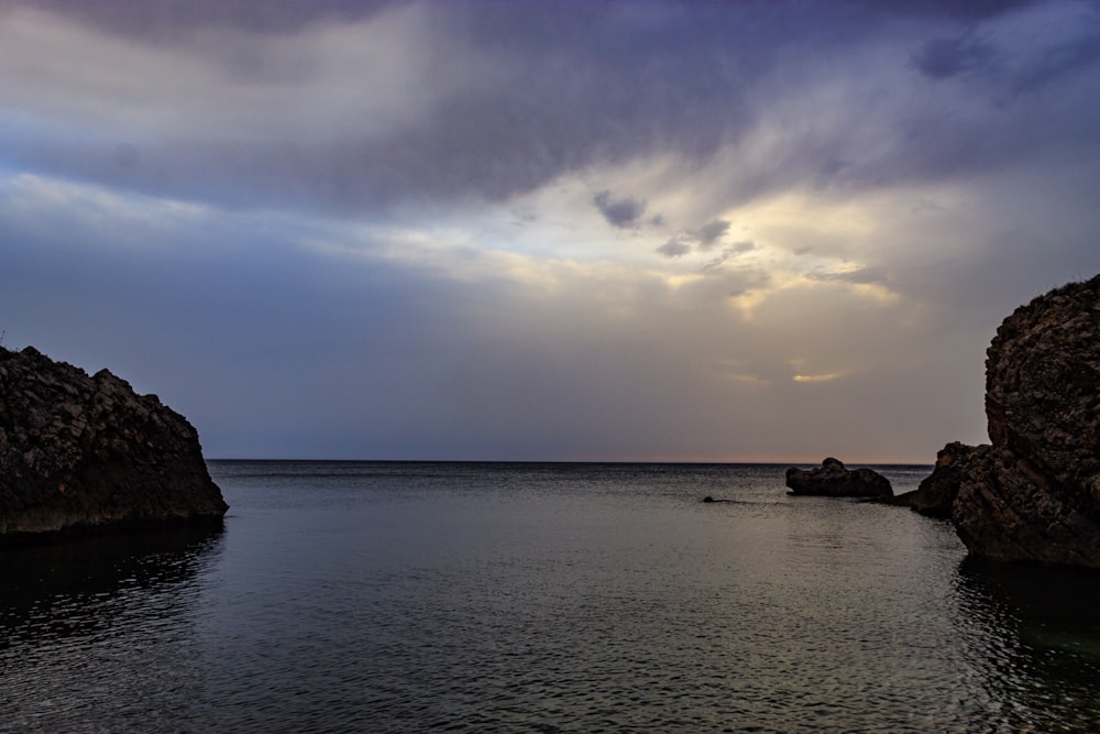 a body of water surrounded by rocks under a cloudy sky