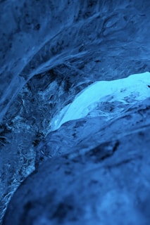 A stunning view of deep blue ice formations with intricate textures and layers. The interplay of light and shadow creates a luminous and almost ethereal quality.