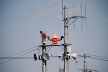 Several utility poles are equipped with various communication devices like loudspeakers, antennas, and a red alert siren. The poles are connected by a network of wires against a clear blue sky.