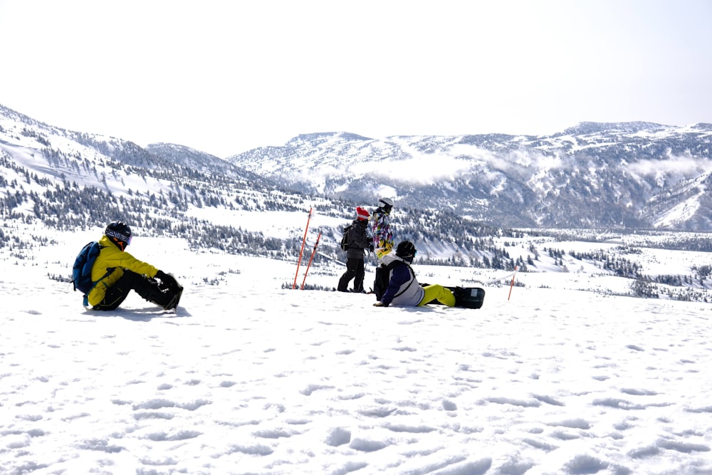 a group of people sitting on top of a snow covered slope