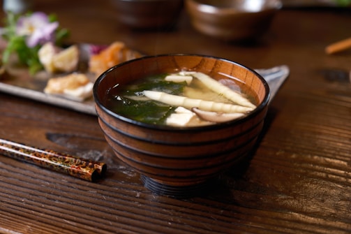 A close-up of a steaming bowl of miso soup with animated-style chopsticks resting on the bowl.