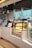 A cafe counter displaying a selection of pastries and beverages with illuminated menu boards above. There is a glass display case housing croissants and bottled drinks, including Coca-Cola. Modern hanging lights provide a soft ambiance.