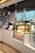A cafe counter displaying a selection of pastries and beverages with illuminated menu boards above. There is a glass display case housing croissants and bottled drinks, including Coca-Cola. Modern hanging lights provide a soft ambiance.