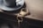 A metallic cup and saucer rest on a wooden surface next to a decorative keychain featuring a golden scorpion design and a set of keys.