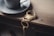 A metallic cup and saucer rest on a wooden surface next to a decorative keychain featuring a golden scorpion design and a set of keys.