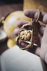 A hand holds a keyring featuring a brass crab-shaped charm and keys. In the background, there is a blurred globe and an open book, suggesting a theme of travel or exploration.