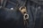 Dark denim jeans featuring a prominent brass keychain shaped like a crab, with a set of keys attached. The fabric's texture and stitching details are visible, highlighting the contrast between the dark denim and the golden keychain.
