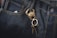 Dark denim jeans featuring a prominent brass keychain shaped like a crab, with a set of keys attached. The fabric's texture and stitching details are visible, highlighting the contrast between the dark denim and the golden keychain.