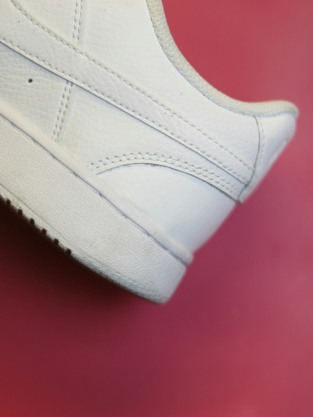 a close up of a white tennis shoe on a red surface