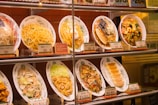 A display case with several plastic food replicas showcasing various dishes, including noodles and dumplings. Each dish is accompanied by a small card with prices and labels in Japanese, indicating typical menu options at a restaurant.