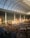 A large indoor amusement park with a high glass ceiling, featuring a monorail track, various colorful attractions, and a crowd of people. The space is spacious and brightly lit, with a whimsical and lively atmosphere.