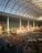A large indoor amusement park with a high glass ceiling, featuring a monorail track, various colorful attractions, and a crowd of people. The space is spacious and brightly lit, with a whimsical and lively atmosphere.