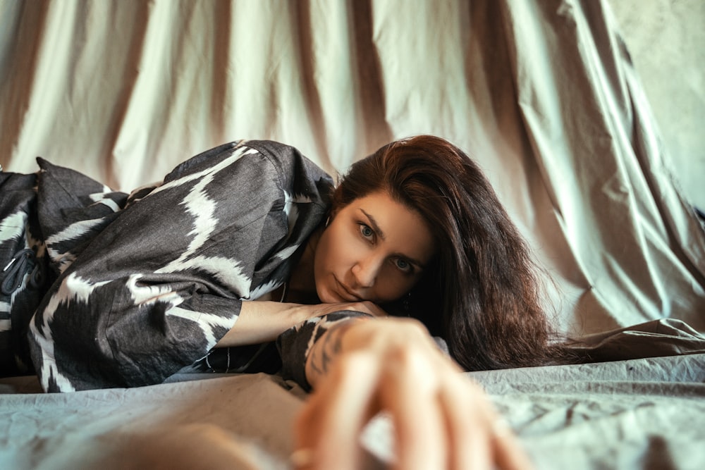 a woman laying on top of a bed next to a curtain