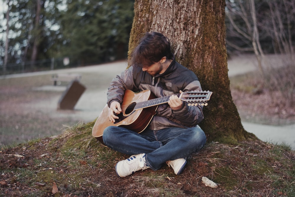 Foto Un hombre sentado bajo un árbol tocando una guitarra – Imagen Música  gratis en Unsplash