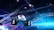 A large indoor arena is equipped with advanced lighting and audio systems. Suspended above the space are numerous digital displays showcasing numbers. The environment is filled with blue illumination and spotlights creating a vibrant atmosphere.