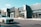 A modern commercial building with clean architectural lines, dark green accents, and large glass windows. A luxury white car is parked in front of the building, which features a sign that reads 'La Rouge'. There are a few plants and light posts along the walkway.