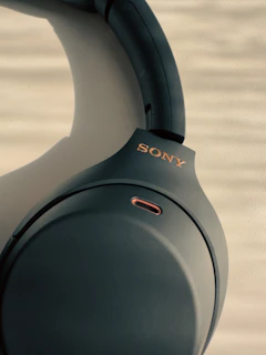 Close-up of a sleek black and gold wireless headphone resting on a smoky, illuminated studio console.