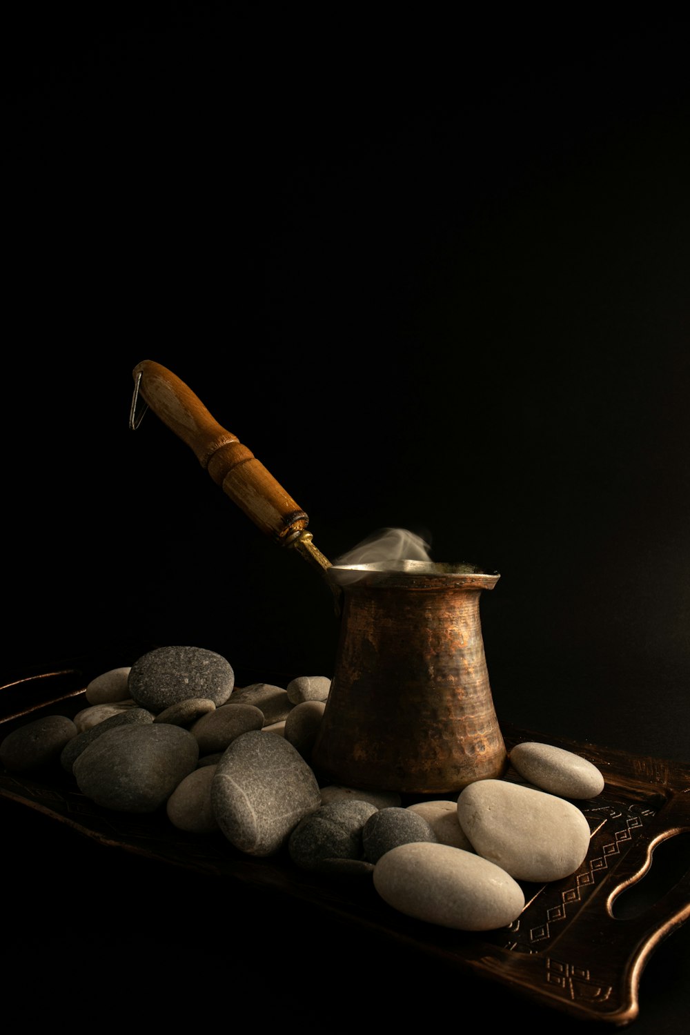 a metal pot sitting on top of a wooden tray filled with rocks