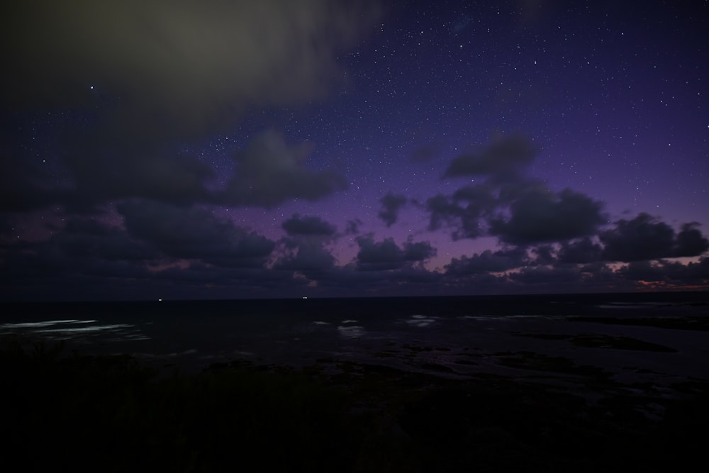 a night sky with stars and clouds over the ocean