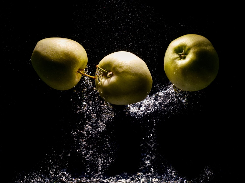 two green apples falling into water on a black background