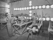 Workers collaborating on electrical wiring in a bright workshop setting.