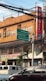 An urban street scene with a building in the background featuring a bank sign. Several green directional road signs indicate directions to Talamban, Cebu City, and Consolacion. Various business signs are visible, including one for Color Options Marketing. There is a parked truck and a car in the foreground. A bundle of overhead wires hangs above the street.