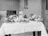 A black and white photograph of a table set with various foods including large cuts of meat, a pitcher of milk, eggs, and a variety of fruits and vegetables such as cauliflower, apples, and turnips. These items are displayed on plates and arranged neatly across a tablecloth.