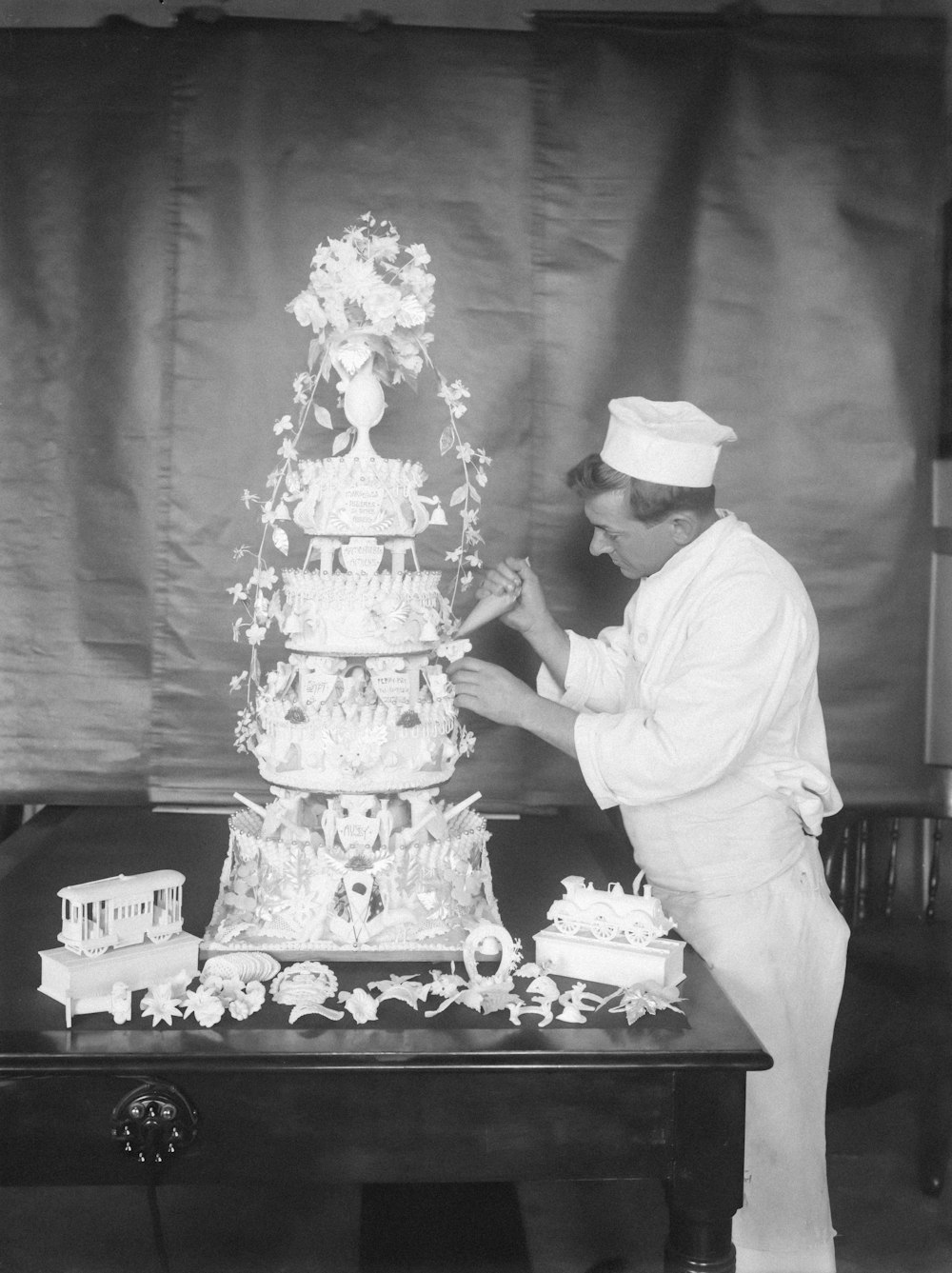 a black and white photo of a man decorating a cake