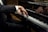 A person dressed in a black suit is playing a grand piano, focusing on the hands and keys. The sleeve has three buttons. The piano is a Steinway & Sons model with a shiny black surface reflecting the player’s hands.
