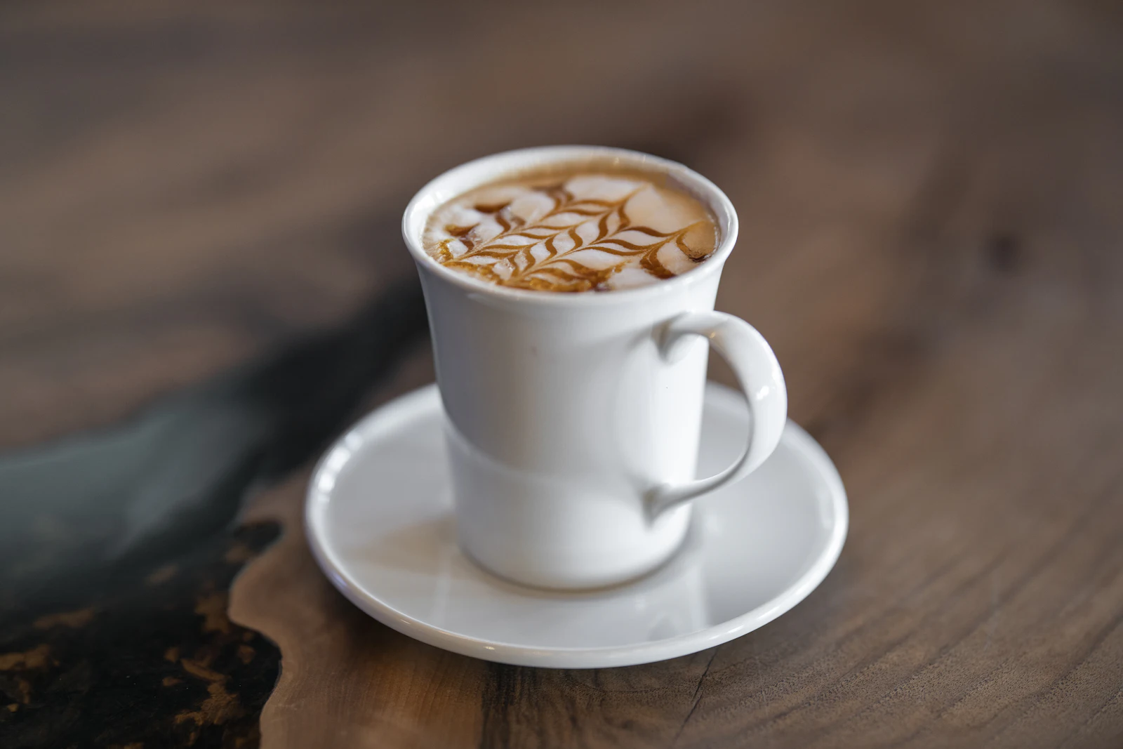 A latte in a cup on a saucer on a warm wooden cafe table
