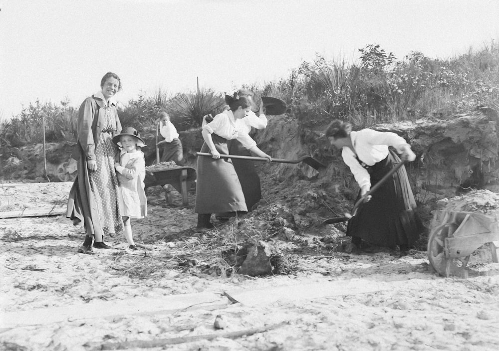 a black and white photo of a group of people digging in the sand