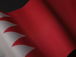 A close-up of a flag featuring alternating red and white zigzag patterns, with rich fabric texture visible across a draped surface.