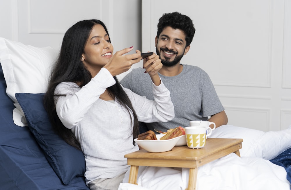 a man and woman sitting on a bed eating food
