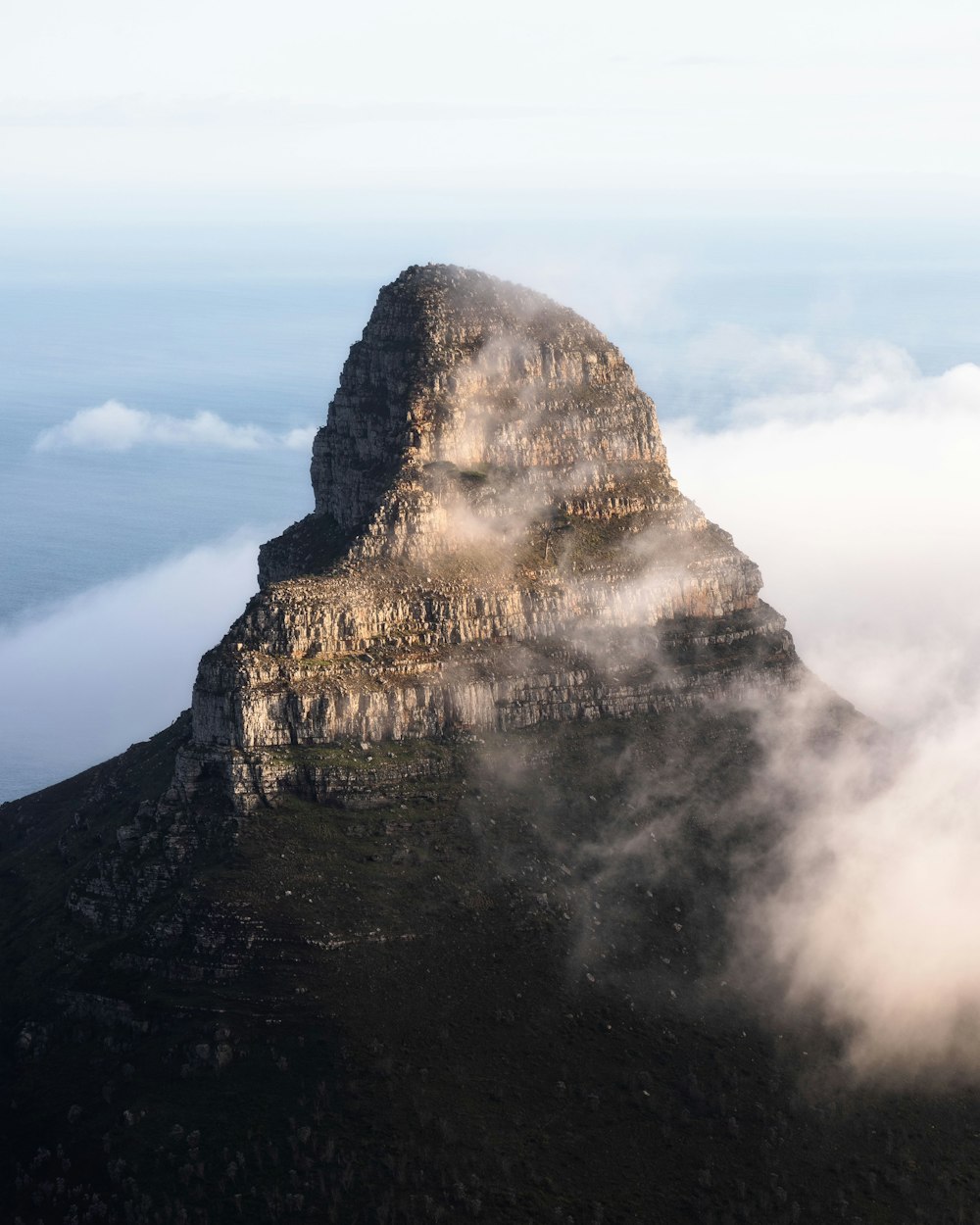 a very tall mountain surrounded by clouds in the sky