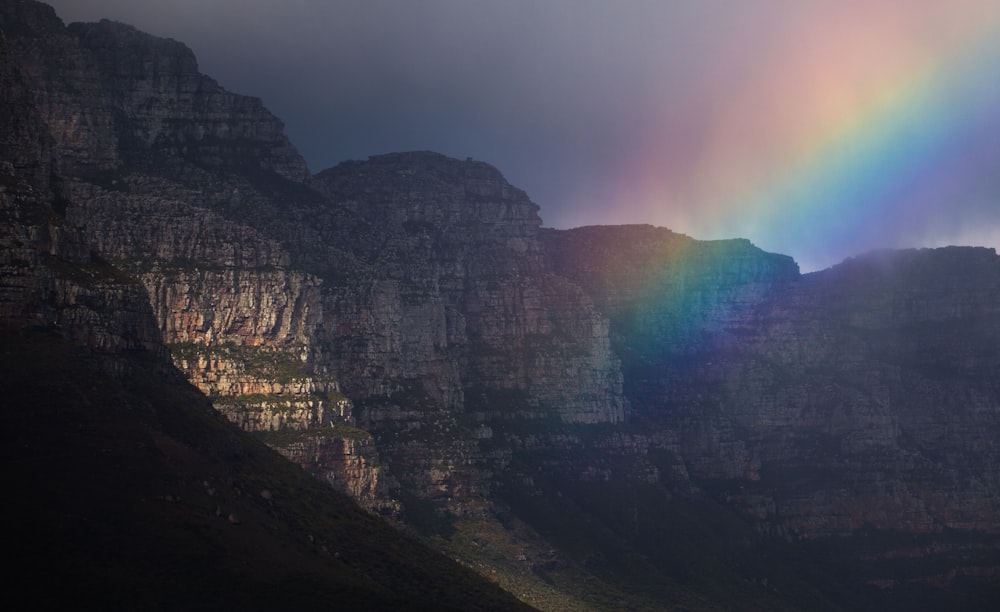 a rainbow shines in the sky over a mountain range