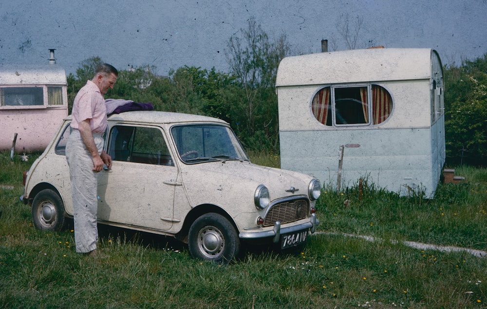 a man standing next to an old car in a field