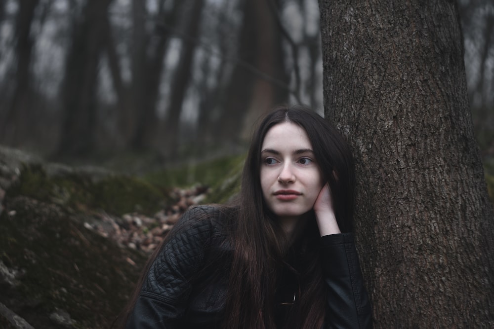 a woman leaning against a tree in the woods